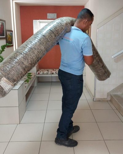 Profissional da T&H Wash carregando tapete enrolado com cuidado e segurança
